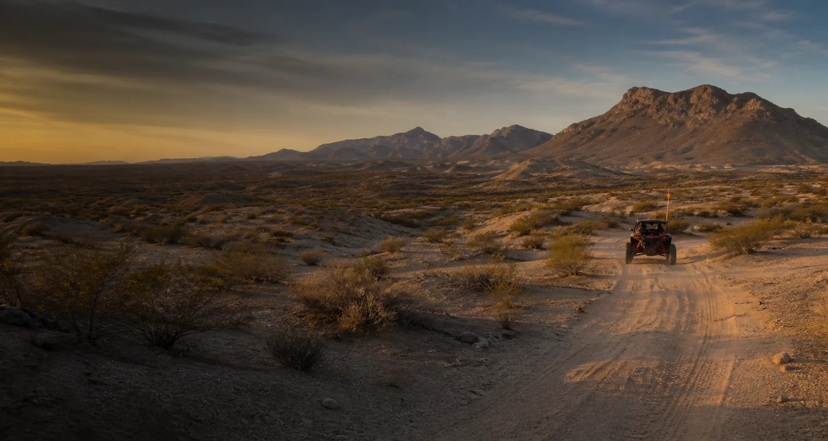 Side-by-side traveling a sandy Hot Well desert trail toward rugged Arizona mountains at golden hour