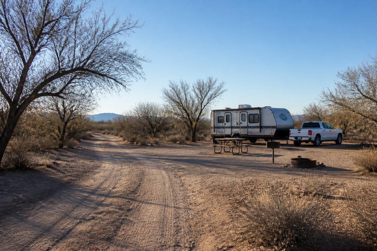 A sparse designated pullout at Hot Well Dunes with clear firm ground, a picnic table, and low desert scrub around it