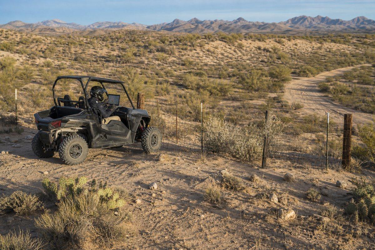 A side-by-side rider stopped inside a desert boundary fence while checking an offline map before continuing